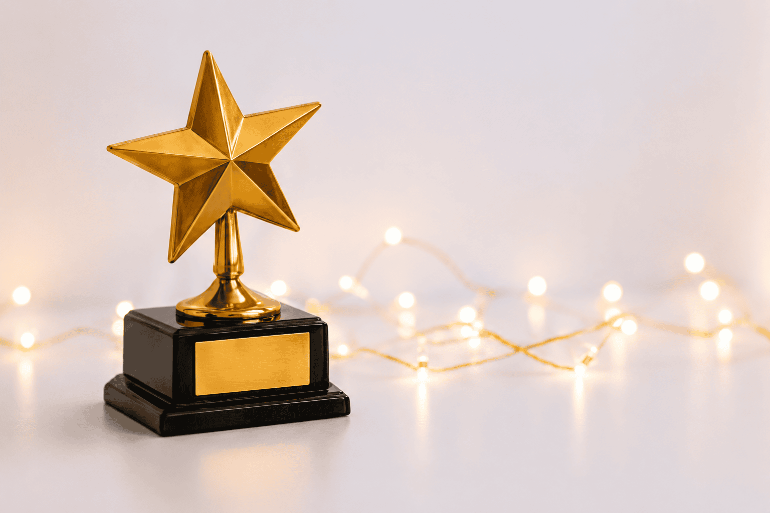 Gold star trophy on a black base with warm fairy lights in the background.